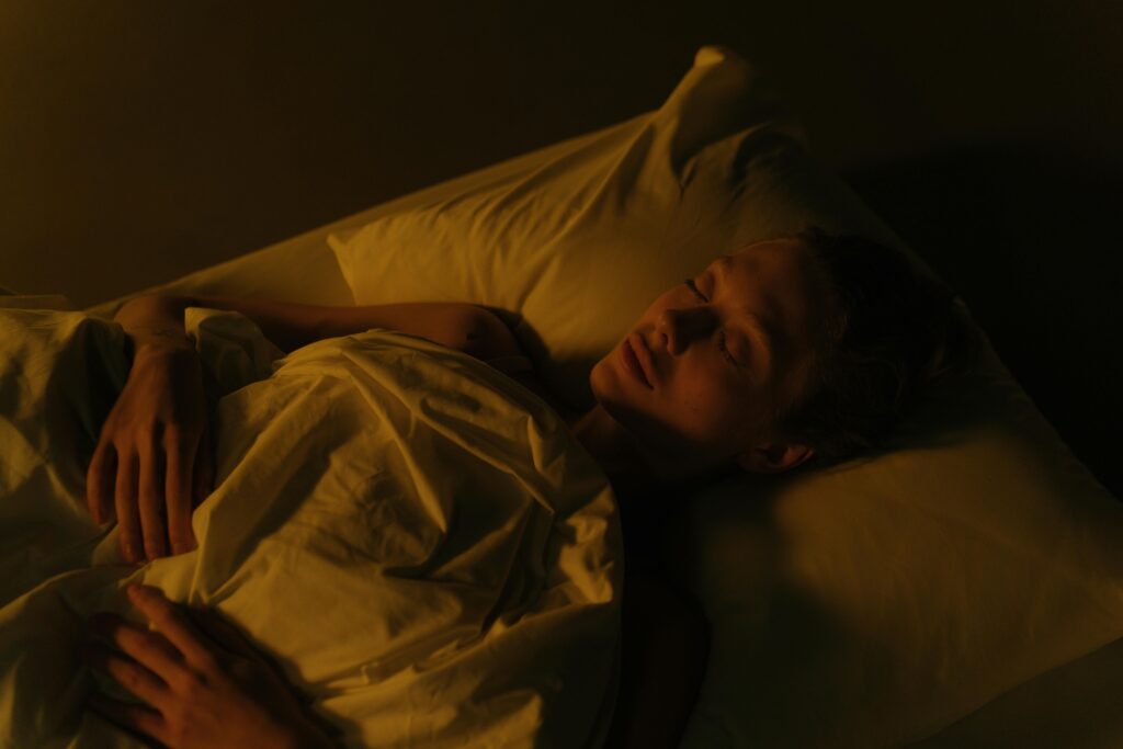 A woman peacefully sleeping in a dimly lit bedroom, wrapped in a white blanket.