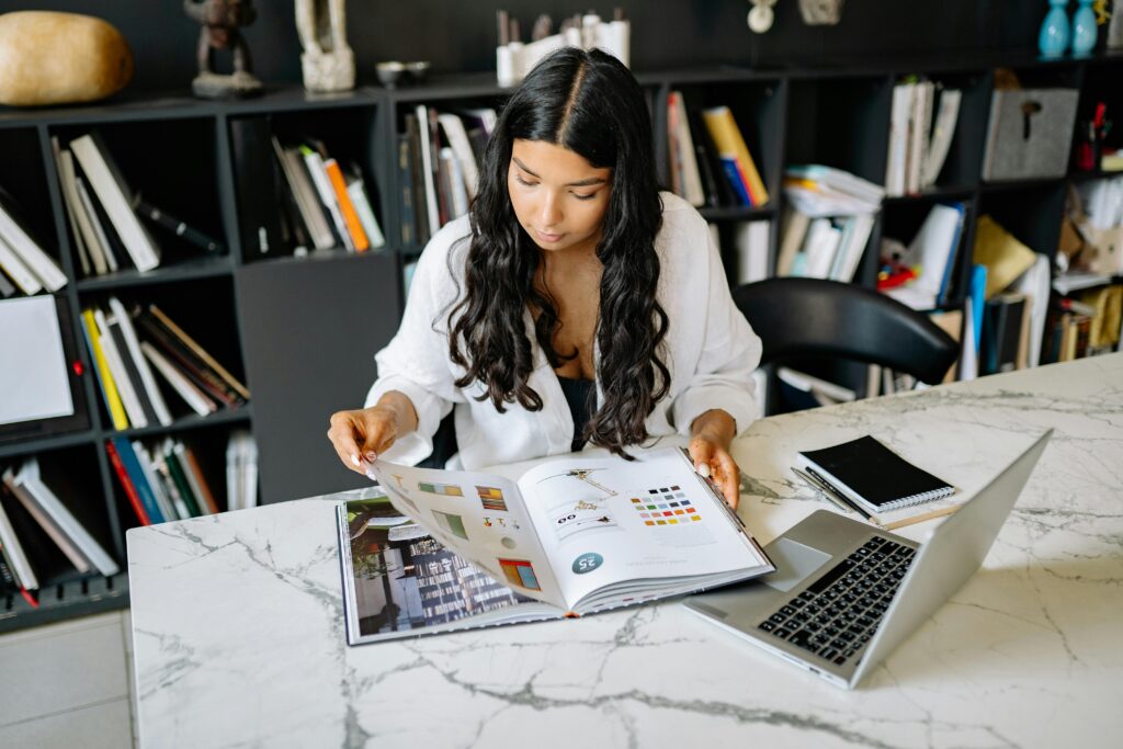 Young woman studying design concepts in a modern office setting with a laptop and books.