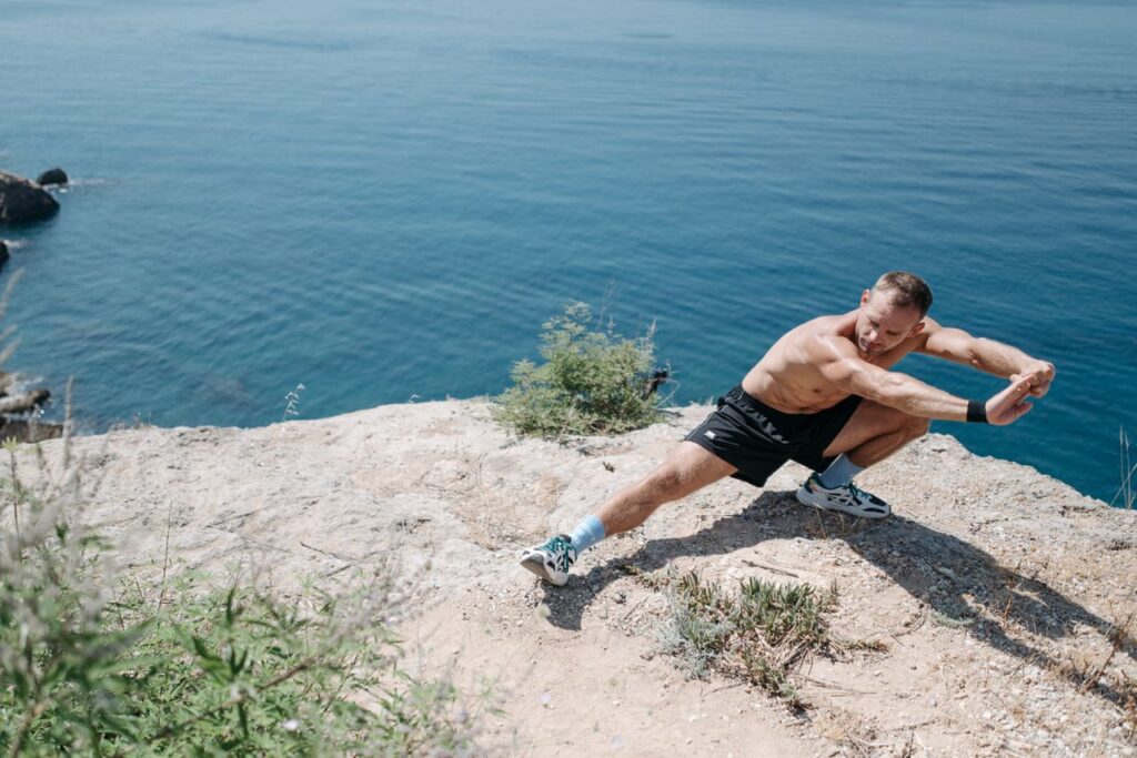How to Lose Stubborn Belly Fat After 40 Shirtless man doing a stretch on a cliff overlooking the ocean in daylight.